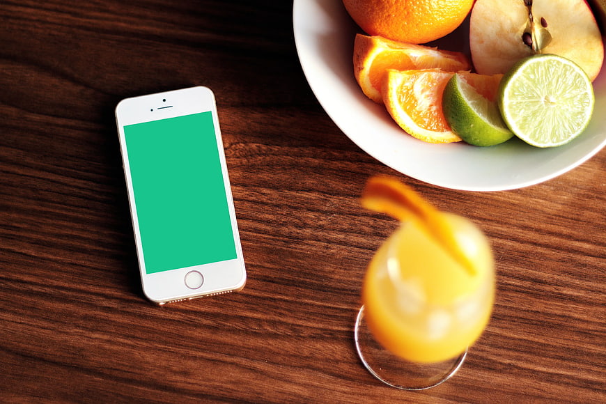 Smartphone with green screen next to fruit bowl and juice