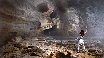 Mystical Woman Standing Before Giant Skull Rock Formation In Cave