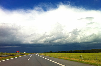 Highway stretching toward dramatic dark storm clouds over green fields