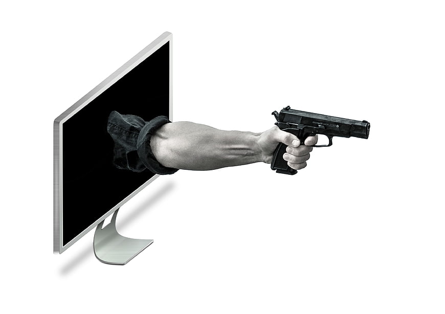 Hand holding gun emerging from computer monitor screen