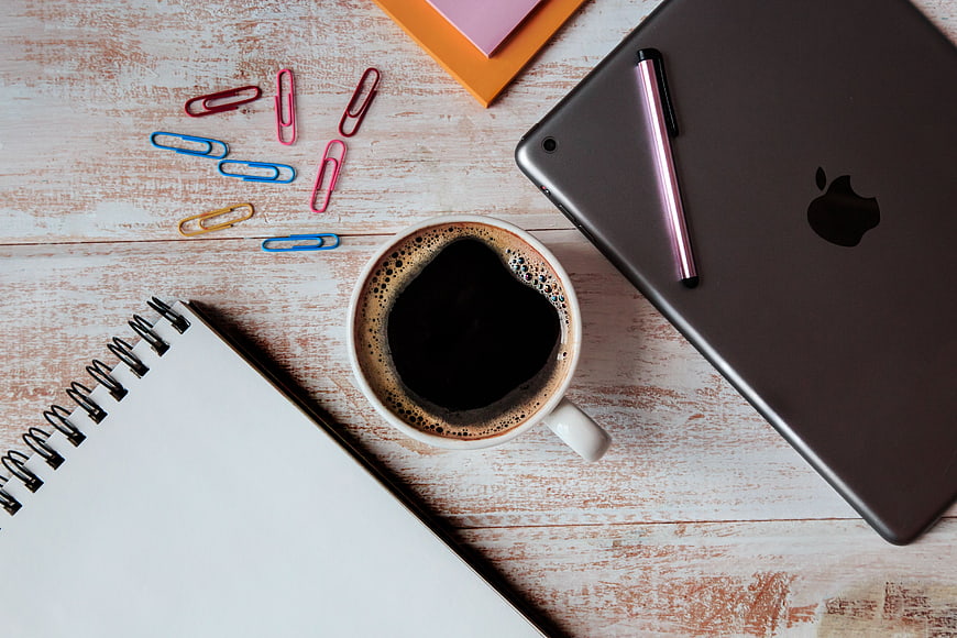 Flat lay workspace with coffee, tablet, and notebook