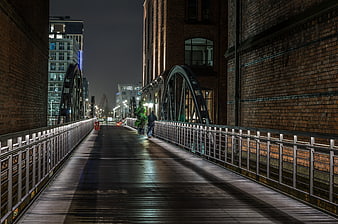 Night view of wooden bridge walkway with brick buildings and city lights