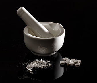 White Porcelain Mortar and Pestle with Crushed Pills on Black Background