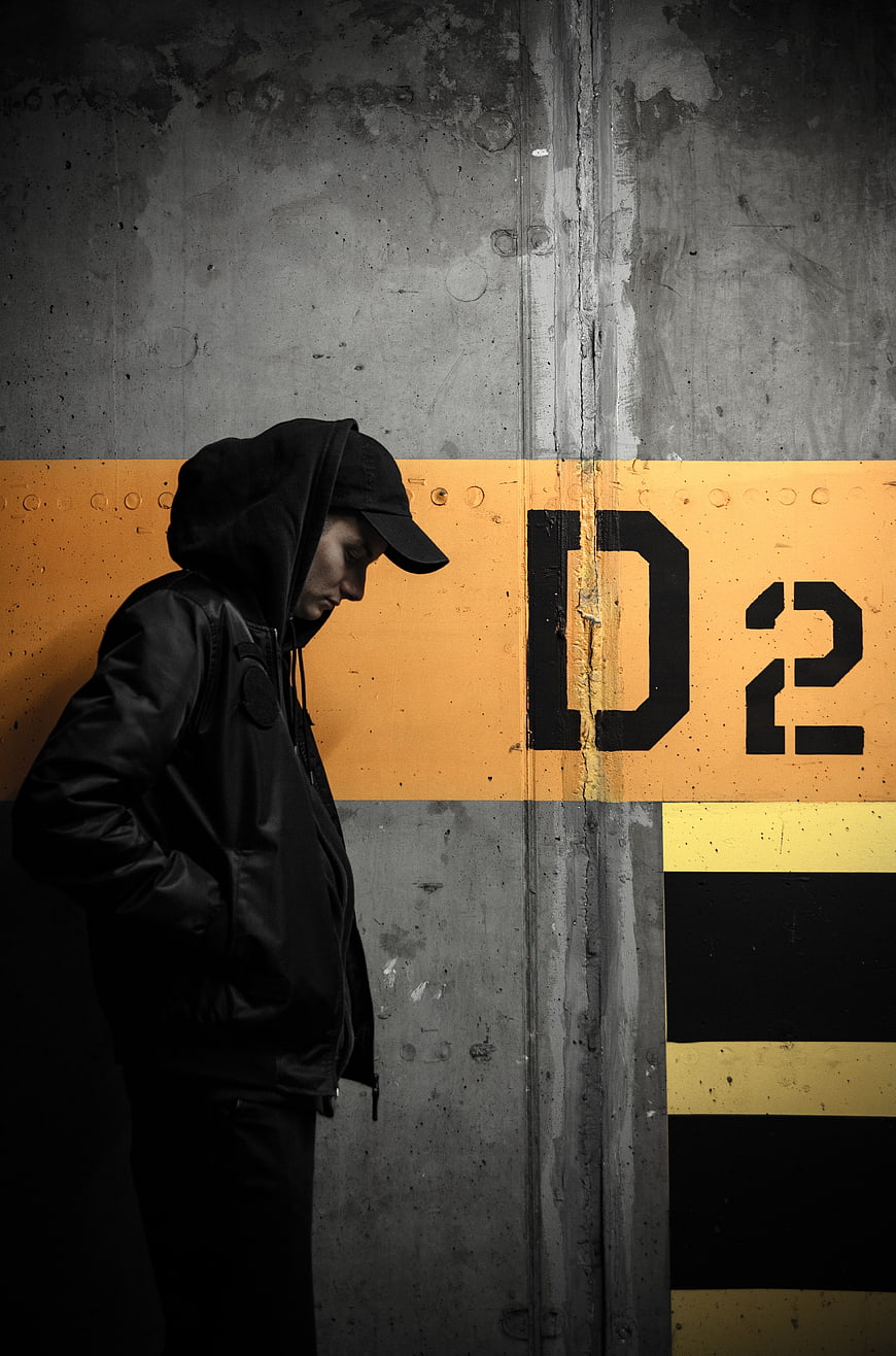 Man in Hoodie Standing Against Concrete Wall with Yellow Stripe