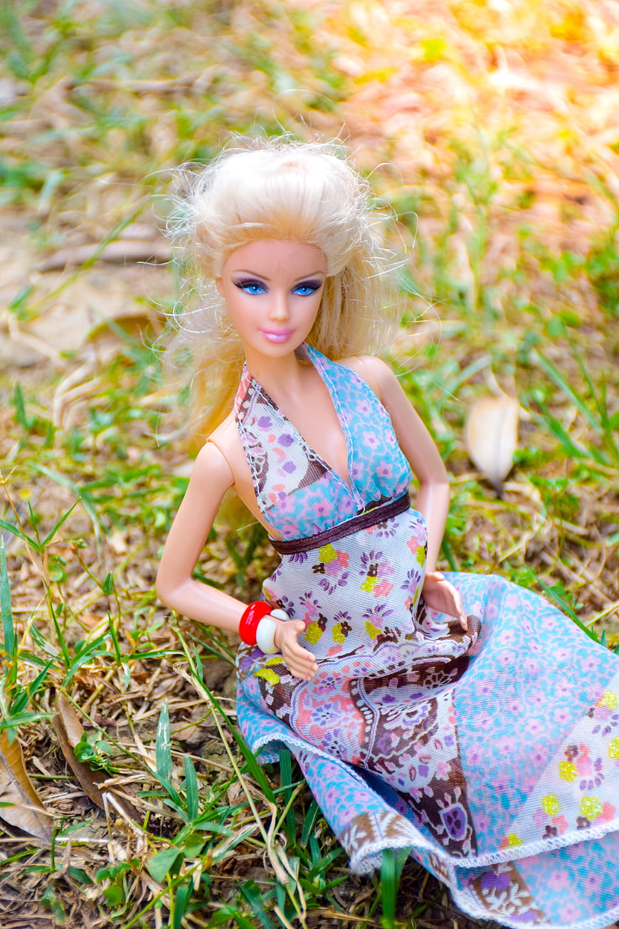 Blonde doll in floral dress sitting on grass