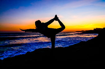 Silhouette of woman doing yoga pose on rocky beach at sunset