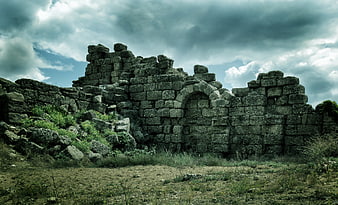 Ancient Stone Ruins with Arched Wall Under Dramatic Cloudy Sky