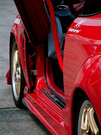 Close-up of red modified sports car with open door and gold wheels