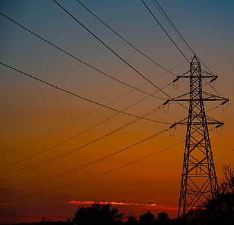Silhouette of electricity pylon against vibrant orange sunset sky