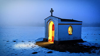 Small white chapel with warm light in snowy winter landscape