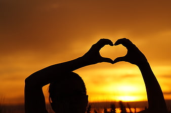 Silhouette of woman making heart shape with hands at sunset