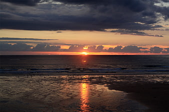 Dramatic sunset over ocean with birds on wet sandy beach
