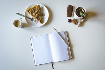 Flat lay of open notebook, coffee, and crumble cake on white desk