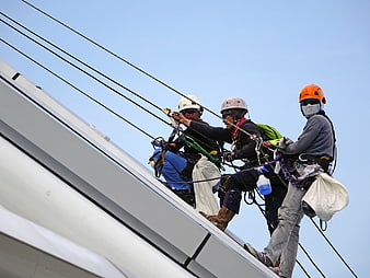 Workers rappelling on a white structure with safety ropes