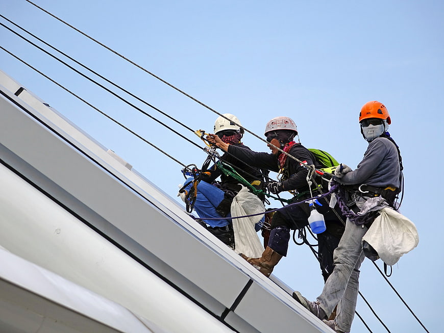 Workers rappelling on a white structure with safety ropes