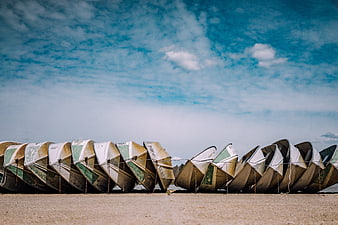 Row of weathered fishing boats on sandy beach under blue sky
