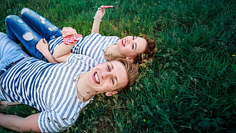 Young couple lying in grass with lollipops
