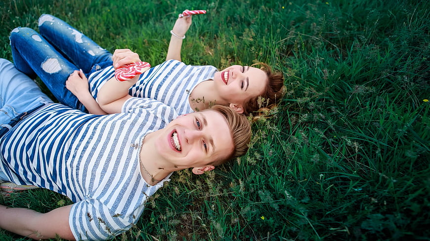 Young couple lying in grass with lollipops