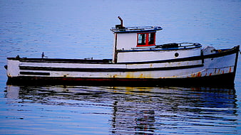 Weathered white fishing boat floating on calm blue water