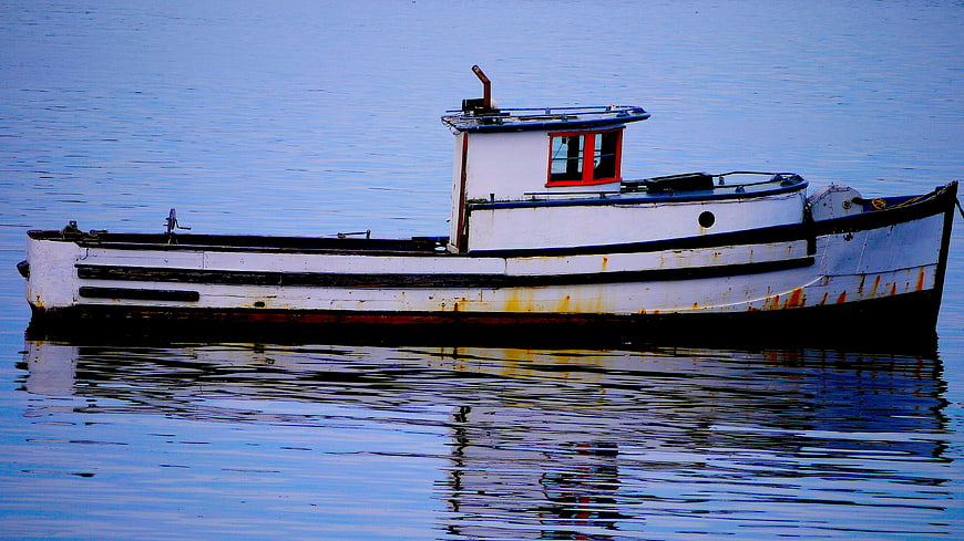 Weathered white fishing boat floating on calm blue water