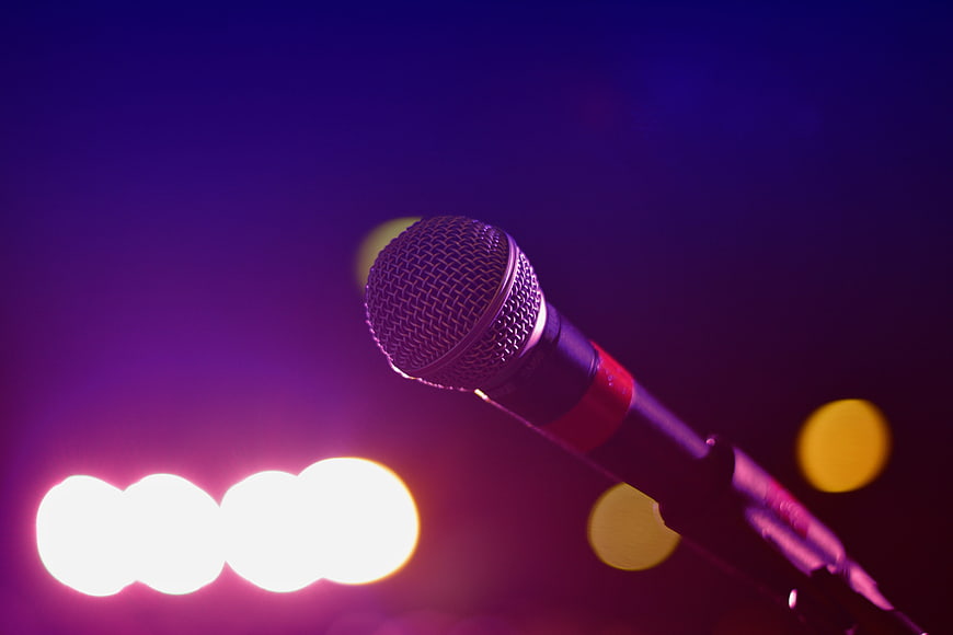 Close-up of a microphone on a stand with purple stage lighting and bokeh