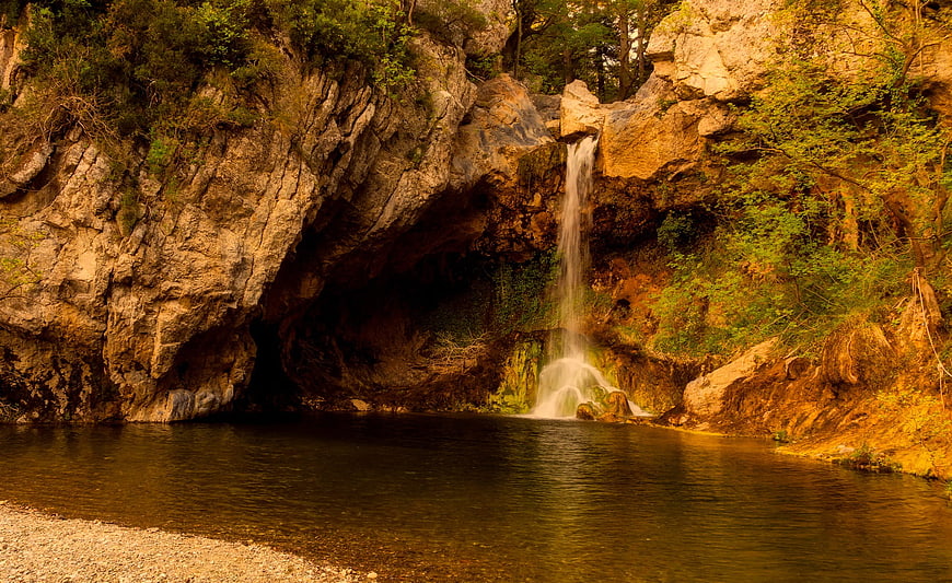 Serene waterfall cascading into a calm river pool surrounded by rocky cliffs