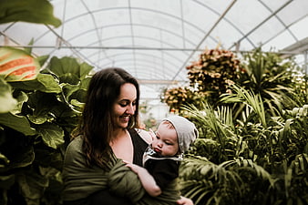 Mother holding baby in lush greenhouse garden