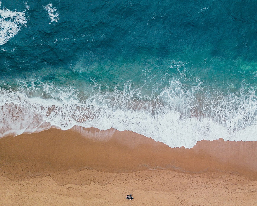 Aerial view of turquoise ocean waves crashing on sandy beach
