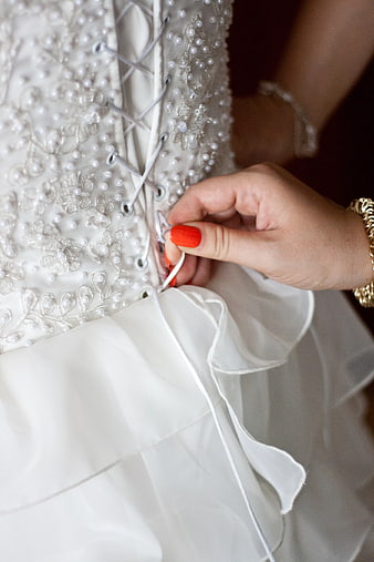 Close-up of hand tying corset back of pearl-embellished wedding dress