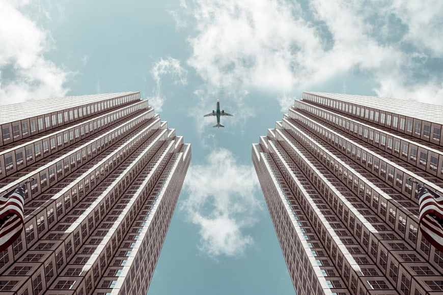 Worm's eye view of airplane flying between skyscrapers