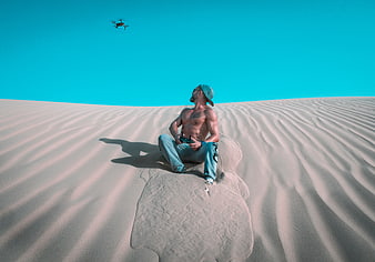 Shirtless Man Flying Drone on Sand Dune