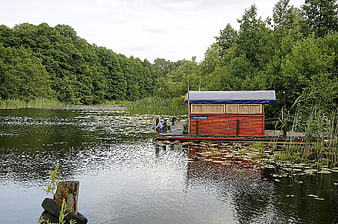 Red wooden boat house on a calm lake surrounded by green forest