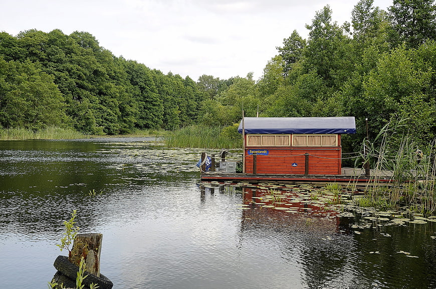 Red wooden boat house on a calm lake surrounded by green forest