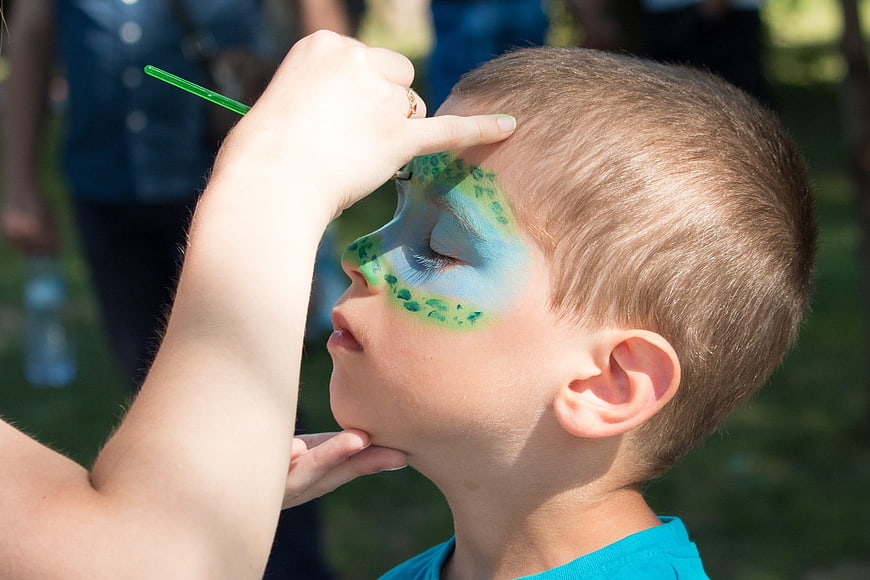Boy Getting Green Face Paint at Outdoor Festival