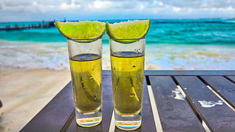 Two Tropical Drinks With Lime Wedges On Beach Table