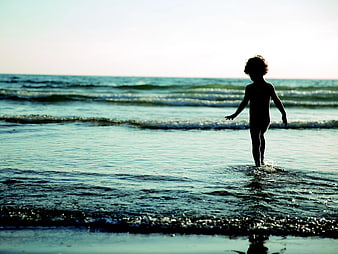 Silhouette of Child Walking in Ocean Waves at Beach
