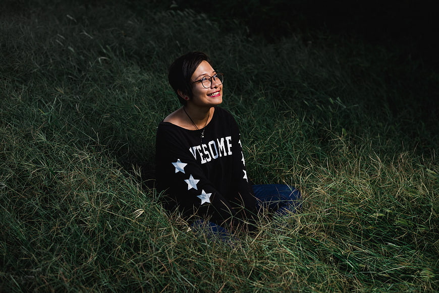 Happy woman with short hair sitting in tall grass