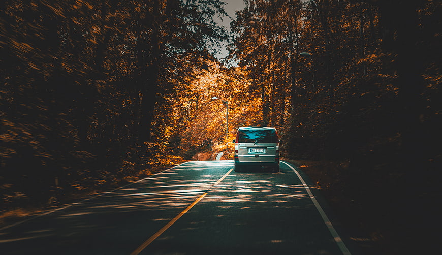 Silver Van Driving on Winding Forest Road in Autumn