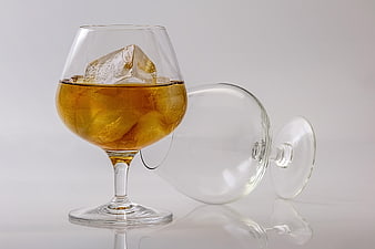 Brandy glass with ice and amber liquid on white background