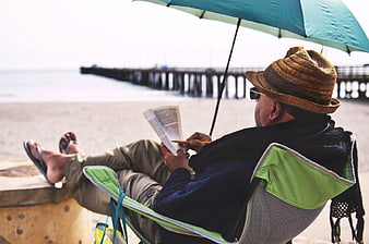Man Reading Book on Beach Chair Under Umbrella