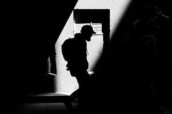 Silhouette of Man Walking Through Dark Alleyway