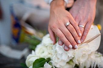 Close-up of wedding rings on hands holding white bouquet