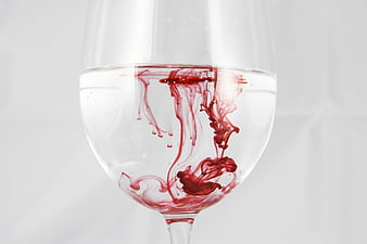 Red ink swirling in a glass of clear water on white background