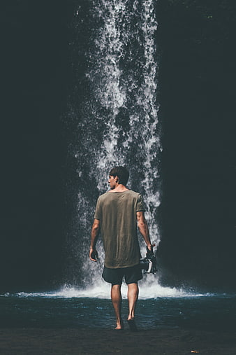 Man with Camera Walking Towards Waterfall in Nature