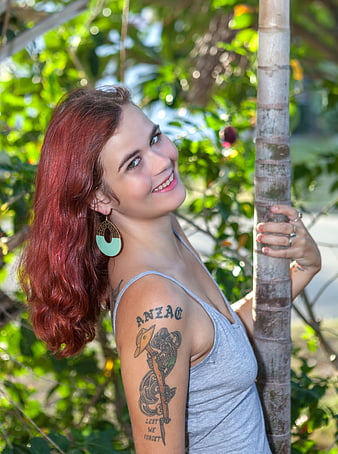 Smiling Redhead Woman with Tattoo Leaning on Tree