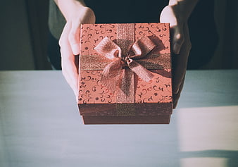 Hands holding a pink gift box with a gold ribbon