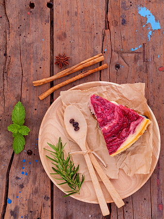 Slice of berry cheesecake on wooden plate with cinnamon and herbs