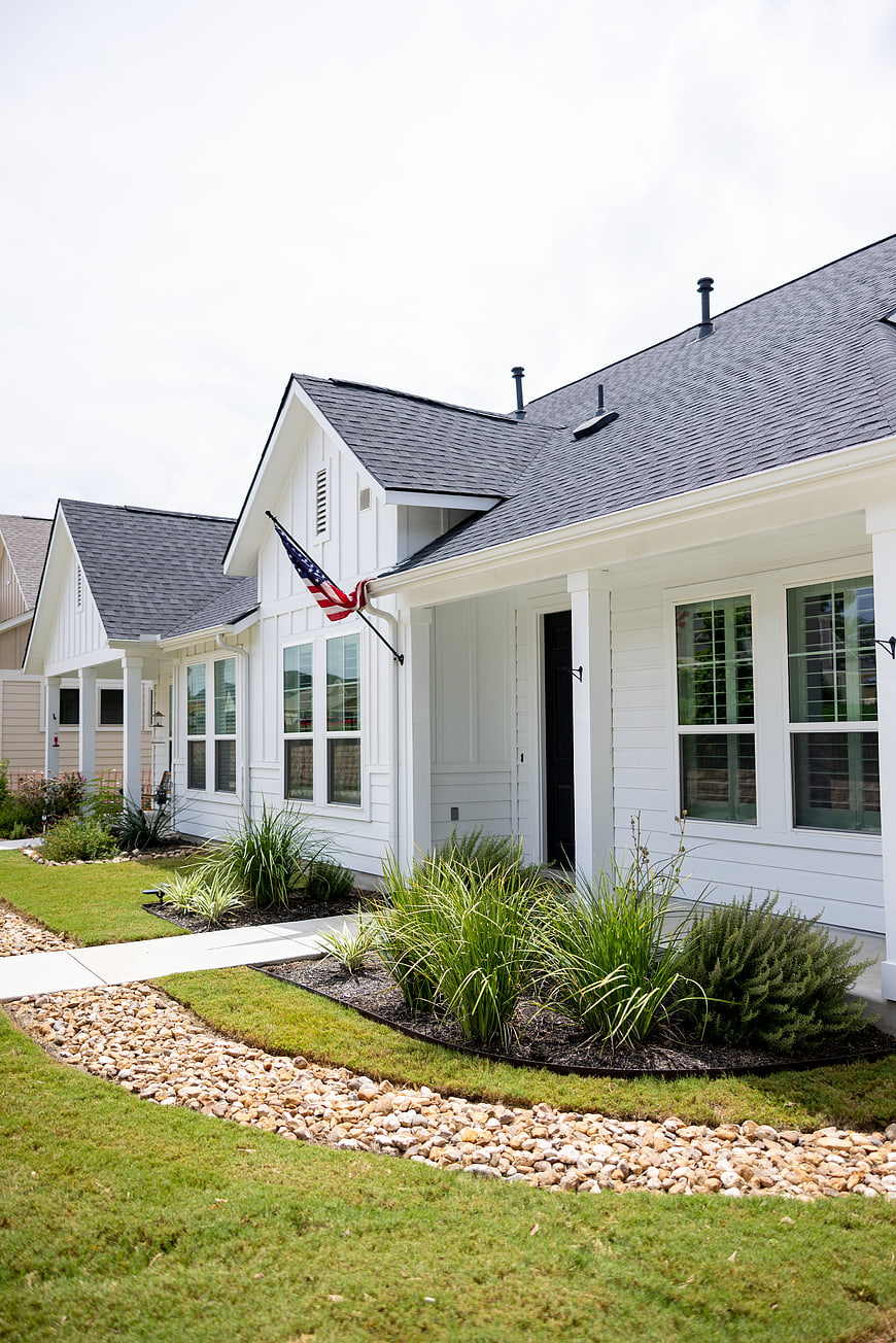 Modern white suburban home exterior with American flag and landscaped yard