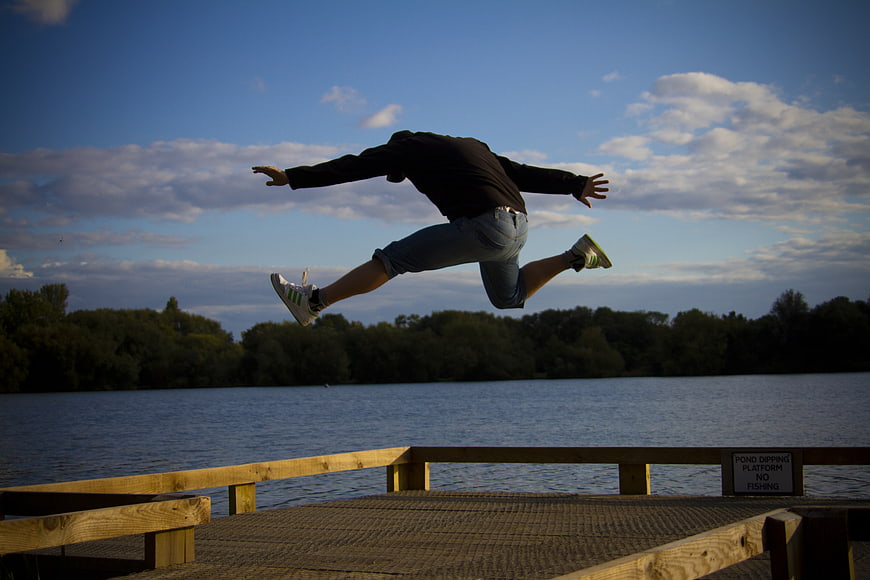 Man Jumping Off Wooden Dock Into Lake