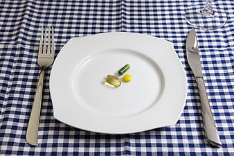 Pills on white plate with cutlery on blue checkered tablecloth